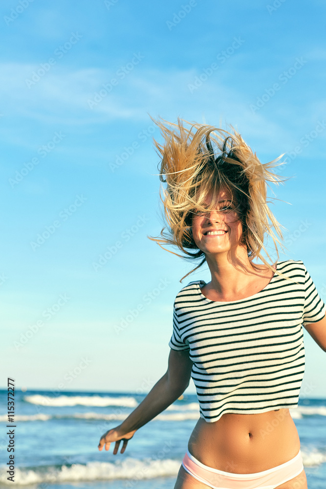 Beautiful woman in swimsuit jumping near the sea. Blonde girl in bikini having fun on vacation. Young woman shakes her hair on a background of the blue ocean.