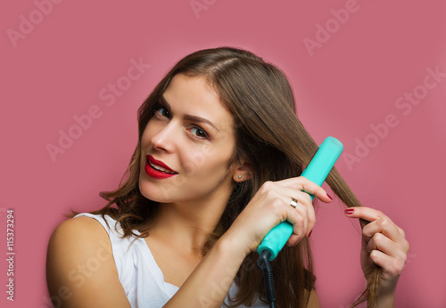 Beautiful woman with a wavy hair holding a hair iron
