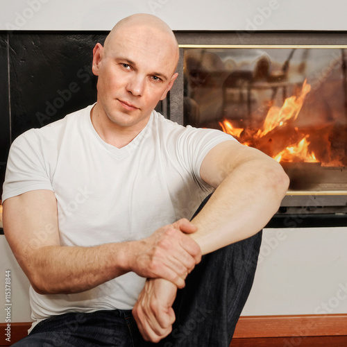 Fotografija Handsome bald headed man sitting on fur carpet at fireplace