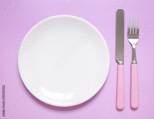 An empty dinner plate, knife and fork on a pink background, arranged as a place setting