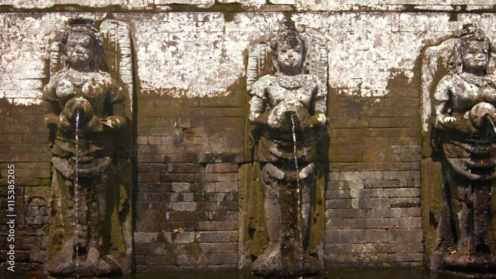 Row of nearly identical, finely detailed stone sculptures of women pouring water from jars into a fountain pool at Tirta Empul Hindu Temple in Bali, Indonesia. Video FullHD Row of nearly identical, finely detailed stone sculptures of women pouring water from jars into a fountain pool at Tirta Empul Hindu Temple in Bali, Indonesia. Video FullHD