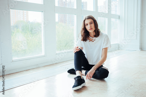 Lost in thoughts. Young beautiful brunette hipster woman sitting on floor near huge window and looking away