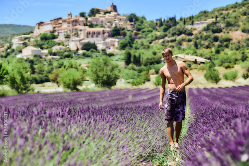 Young man with a naked torso in the lavender flowers. Handsome guy enjoying nature and the beauty of flowers. On the background of green trees and blue sky.
