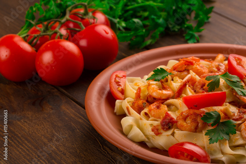 Fettuccine pasta with shrimp tomatoes and herbs. wooden background
