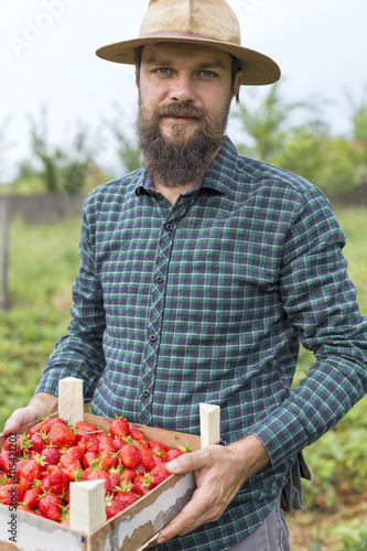 Portrait of young farmer holding a box full with fresh red str