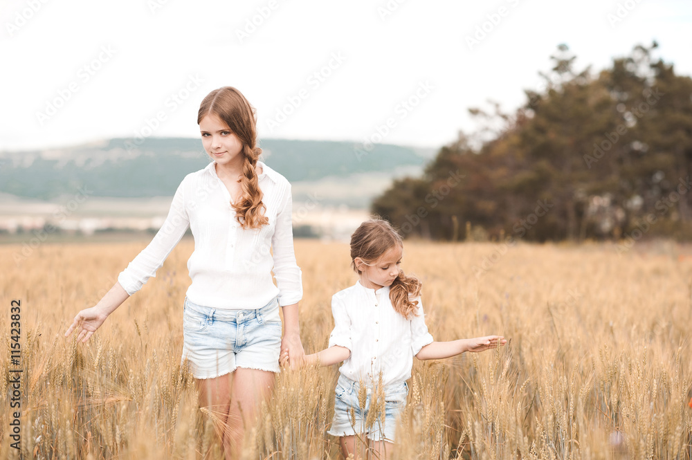 Two sisters in similar clothes walking in rye field outdoors. Togetherness. Friendship.
