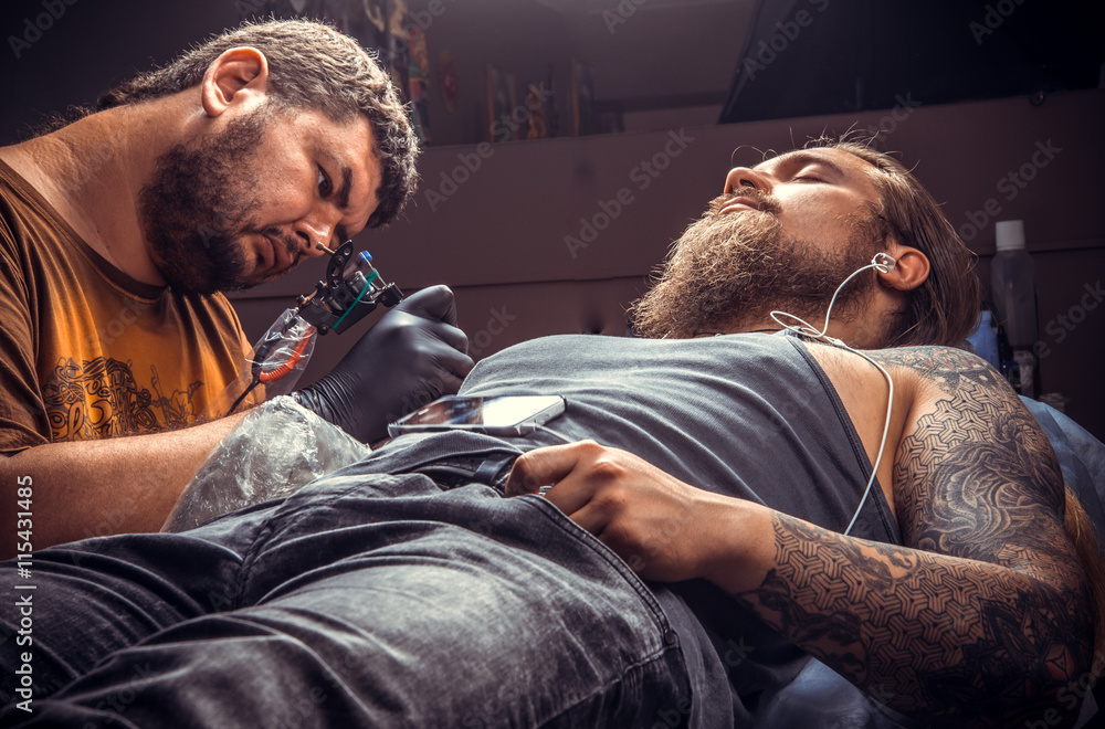 Fototapeta premium Professional tattooer working tattooing in tattoo parlor