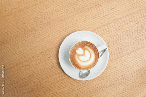 A cup of coffee with heart pattern in a white cup on wooden background
