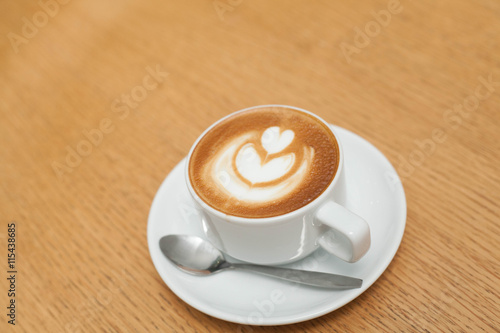 A cup of coffee with heart pattern in a white cup on wooden background
