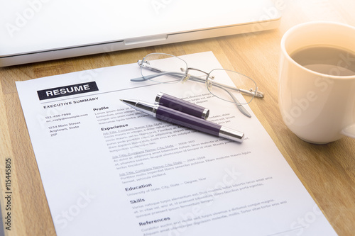 Businessman or job seeker review his resume on his desk before send to finding a new job with pen, computer laptop, glasses, a cup of coffee and smart phone.