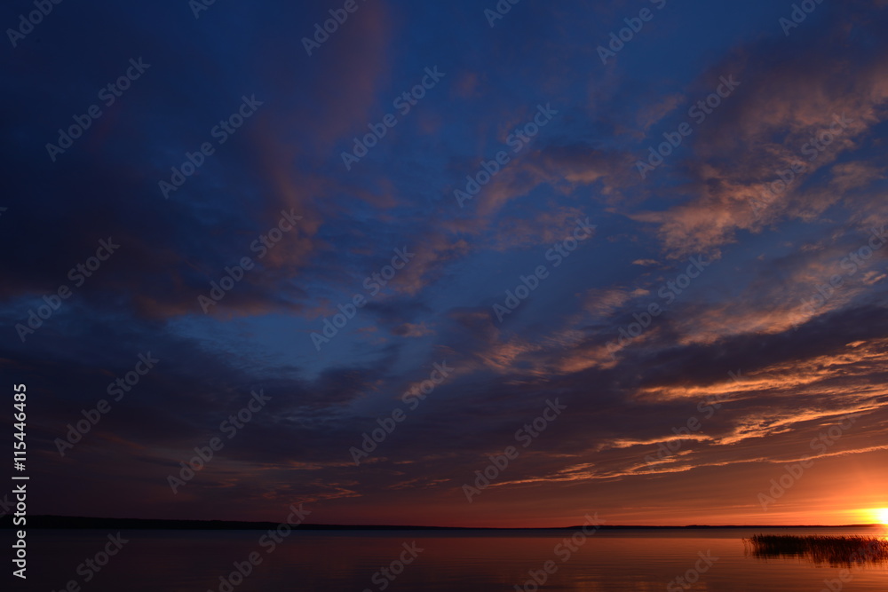 Summer evening sky clouds fall into the lake at sunset
