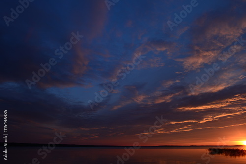 Obraz na płótnie Summer evening sky clouds fall into the lake at sunset w salonie