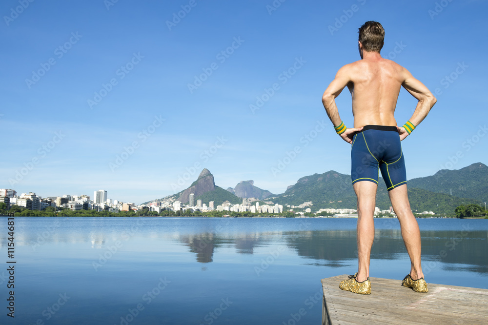 Shirtless athlete in blue compression shorts standing in front of the Rio de Janeiro, Brazil skyline at Lagoa Rodrigo de Freitas lagoon