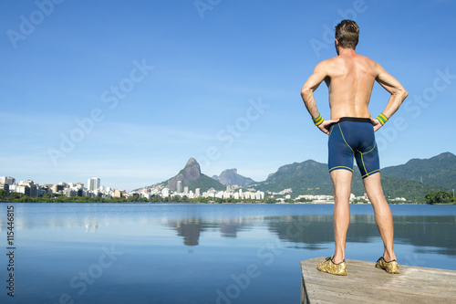 Shirtless athlete in blue compression shorts standing in front of the Rio de Janeiro, Brazil skyline at Lagoa Rodrigo de Freitas lagoon