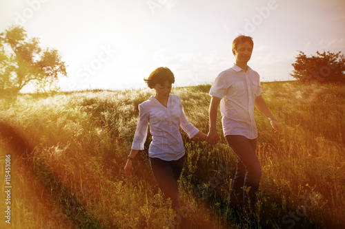 Happy couple holding hands walking through a meadow, tinted photo