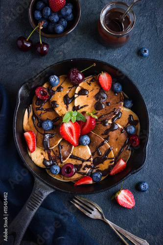 pancakes with fresh berries and chocolate sauce on pan, black ba