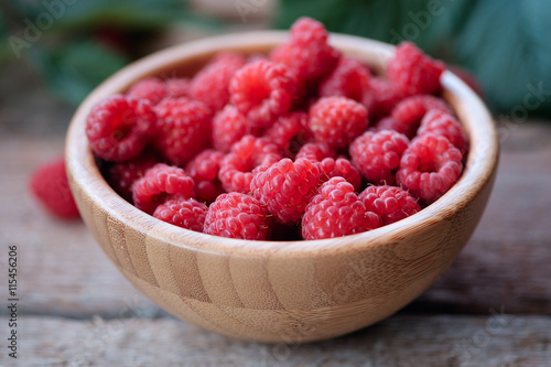 Fresh organic raspberries in bowl wood background.