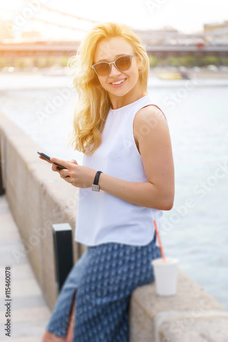 Pretty blond woman in sunglasses with phone near the river