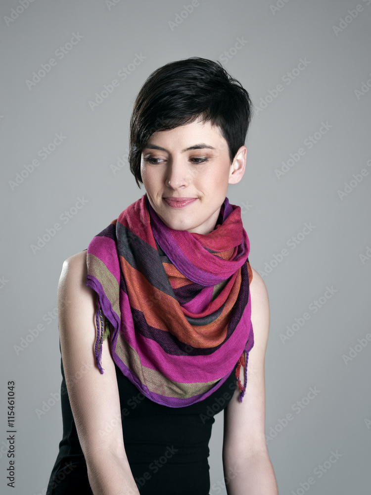 Portrait of pensive smiling short hair woman with colorful shawl looking down over gray studio background. Portrait of pensive smiling short hair woman with colorful shawl looking down over gray studio background.