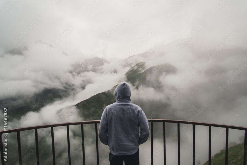 Obraz premium View from behind of a man standing at view point looking to beautiful landscape with foggy mountains in the distance