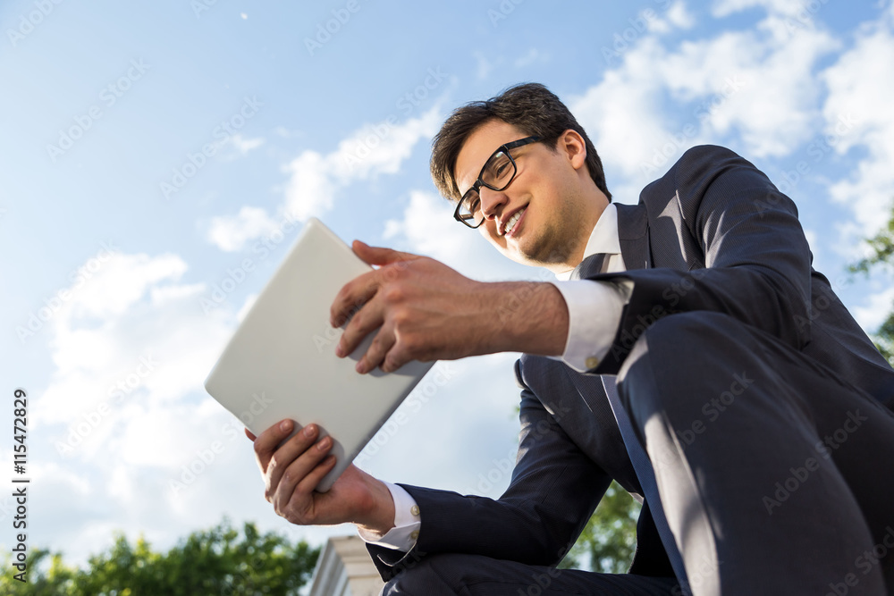 Cheerful businessman using tablet outside