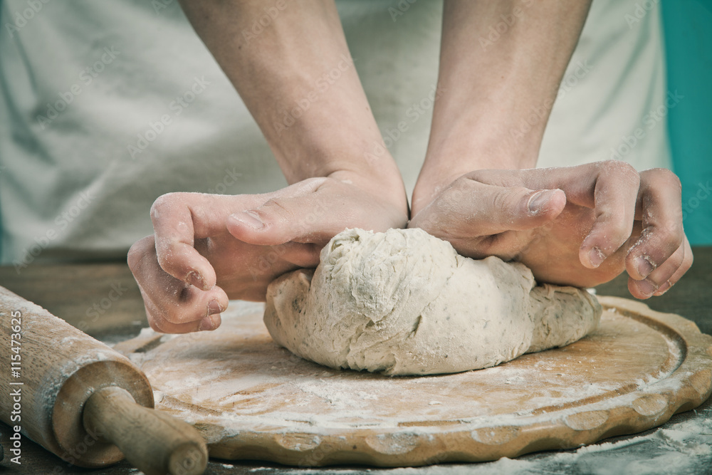 Fototapeta premium Making dough by mens hands on wooden table background