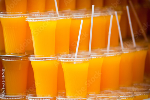 Many plastic glasses with orange juice on stall shop