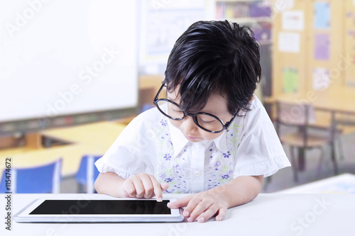 Little girl with glasses uses tablet in class