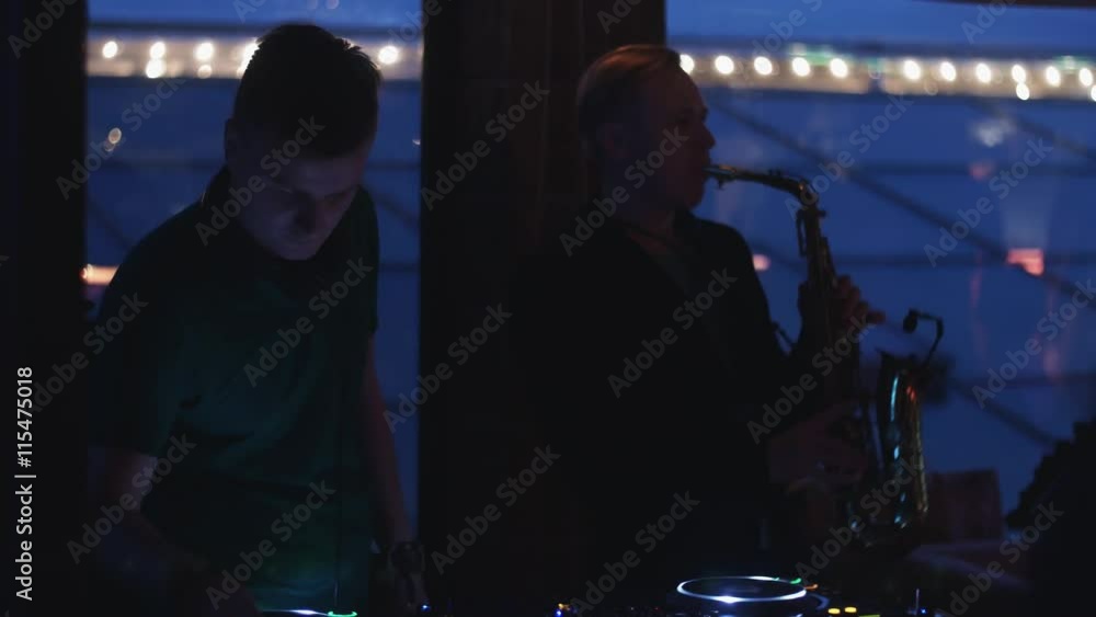 Dj spinning at turntable. Man play saxophone. Party in nightclub. Silhouettes. Music Dj spinning at turntable. Man play saxophone. Party in nightclub. Silhouettes. Music