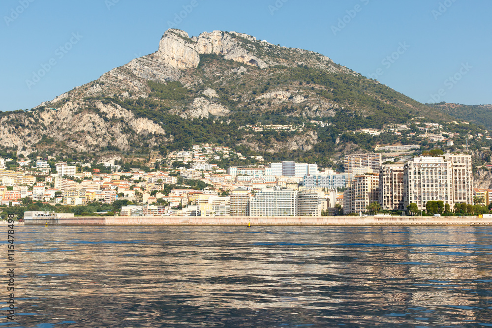 Luxury homes on the rocky Mediterranean coast of the French Riviera at Monte Carlo in Monaco, with mountain in the background. Horizontal with copy space for text