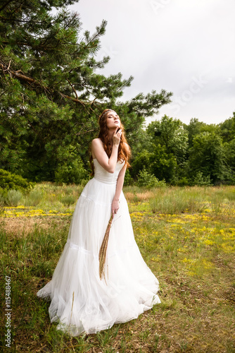 Redheaded young girl in the woods. Portrait of the bride in the Park. A girl holds wheat ears in the hands.