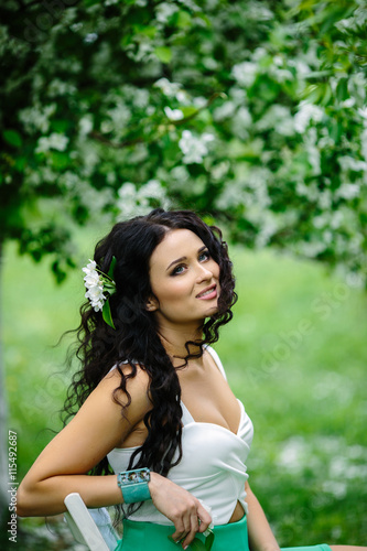 Young brunette woman portrait sitting on white chair in blooming apple tree park