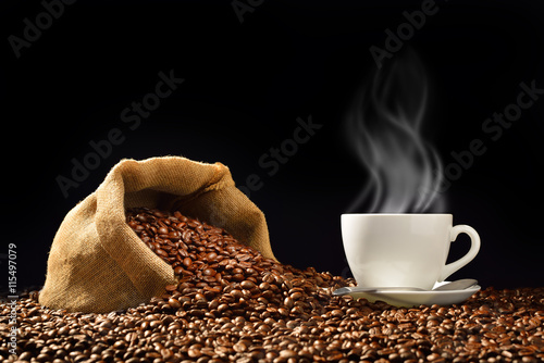 Cup of coffee with smoke and coffee beans in burlap sack on black background