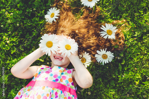 Child with daisy eyes lying on green grass. photo