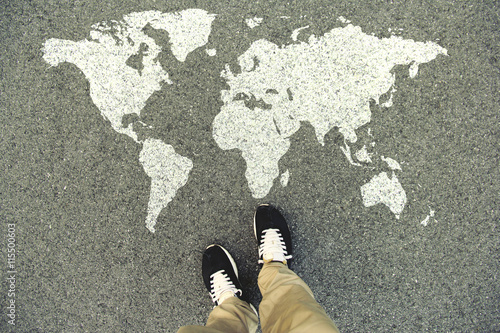 World map on an asphalt road. Top view of the legs and shoes. POV photo