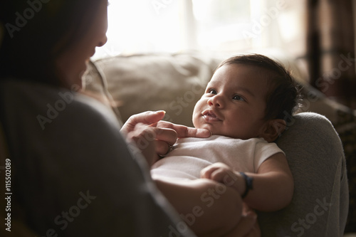 Close Up Of Mother Playing With Baby Boy Lying On Sofa