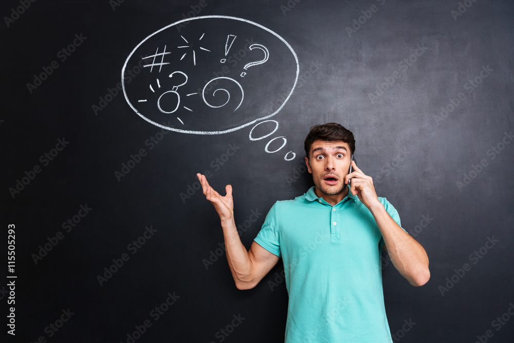 Amazed shocked man talking on mobile phone over blackboard background