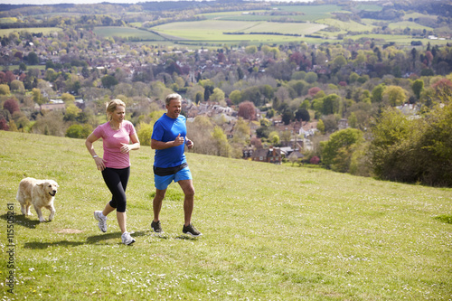 Mature Couple With Golden Retriever Jogging In Countryside photo