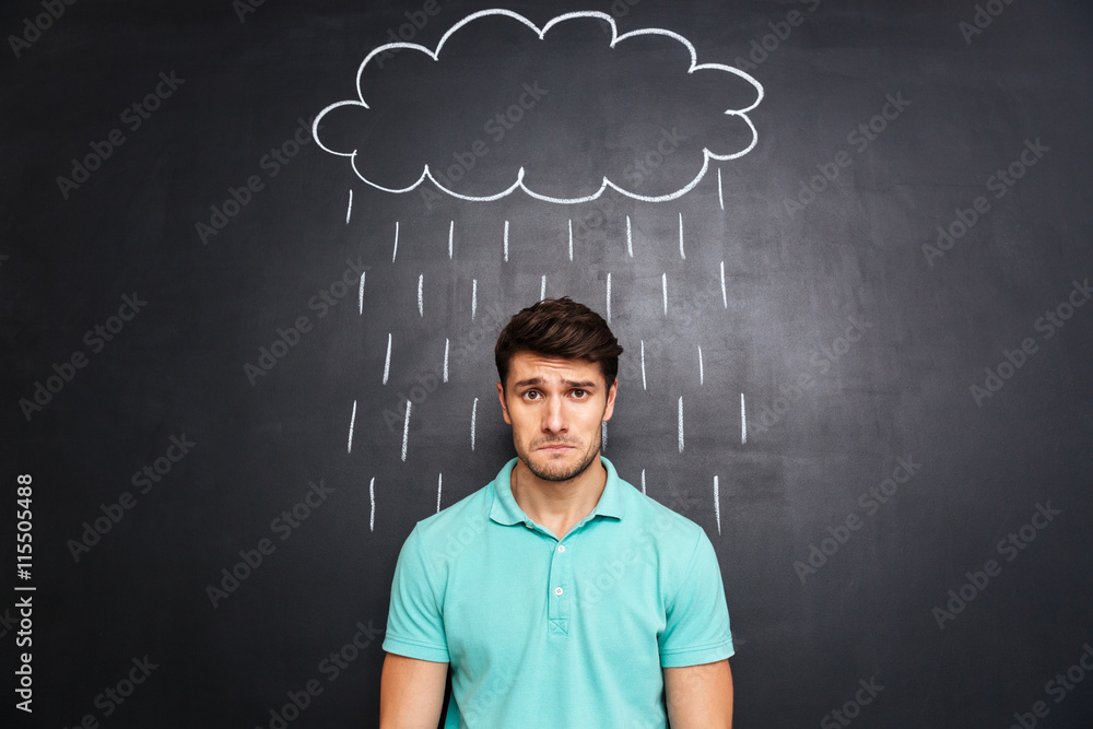 Sad man standing under the rain drawn on blackboard background