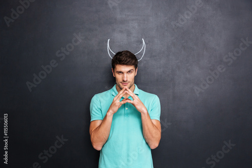 Serious man playing role of devil standing over blackboard background