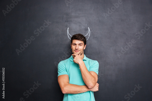 Pensive young man with drawn horns standing and pretending devil