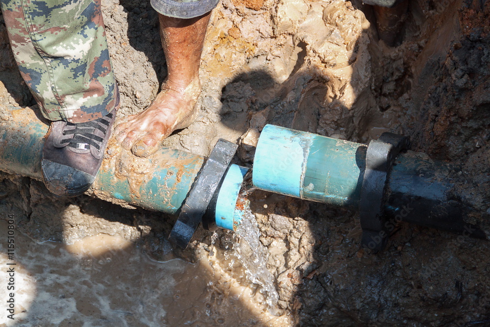Obraz premium plumber workers repair pipe water main broken, tube underground water on road.
