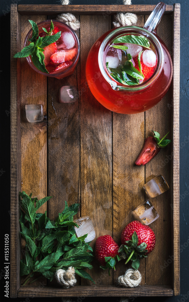 Homemade strawberry lemonade, mint and ice, served with fresh berries on rustic wooden tray over dark background, top view, copy space