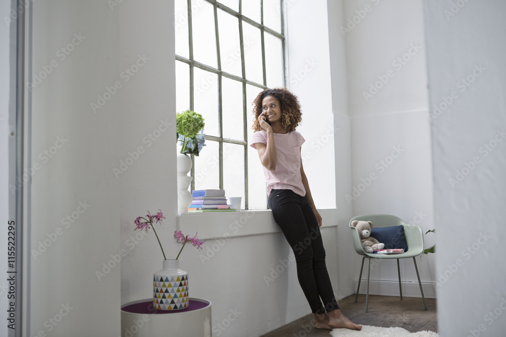 Young woman standing at the window talking on the phone Young woman standing at the window talking on the phone