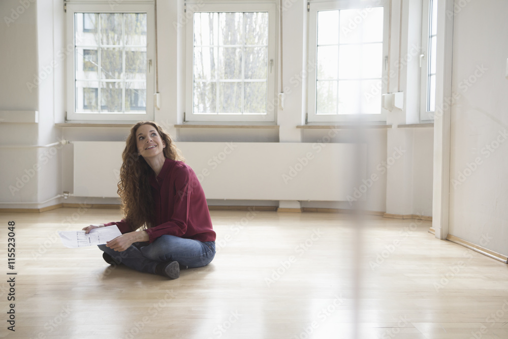 Woman sitting on floor in empty apartment looking around Woman sitting on floor in empty apartment looking around