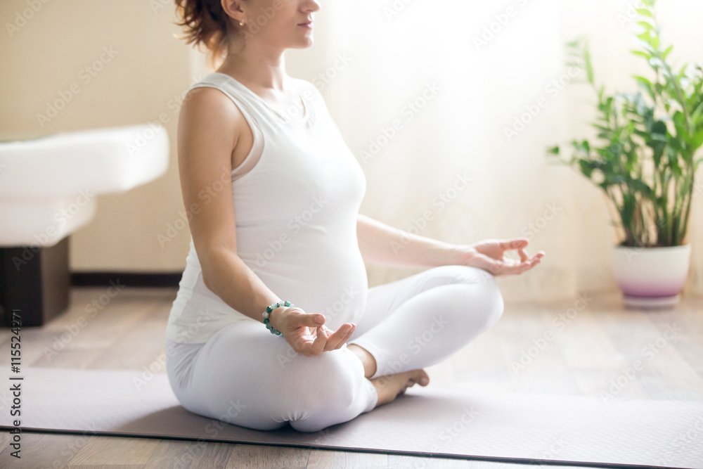 Healthy Pregnancy Yoga and Fitness. Young pregnant yoga woman working out in living room interior. Pregnant model sitting in prenatal easy pose, meditating indoors. Torso close-up