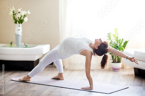 Healthy Pregnancy Yoga and Fitness concept. Young pregnant yoga woman working out in living room. Pregnant model doing prenatal Camatkarasana, Wild Thing or Flip-the-Dog posture yoga backbend exercise
