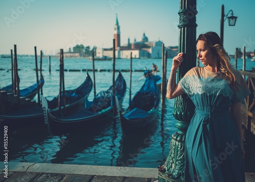 Beautiful well-dressed woman standing near San Marco square with gondolas and Santa Lucia island on the background. 