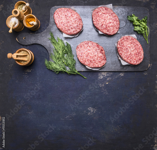 concept of home cooking chops of marble beef four cutlets are laid out on vintage cutting board on a blue rustic wooden background with parsley and dill and spices, space for text top view