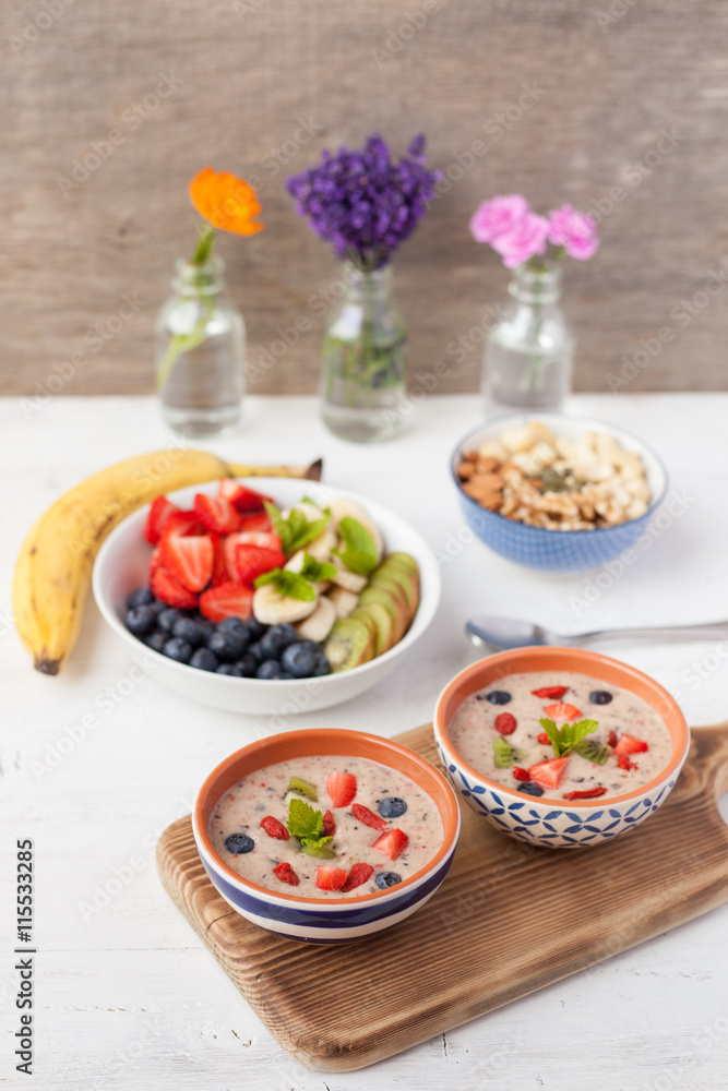 Vegan fruit and berry smoothie breakfast, topped with blueberries, strawberries and mint, seved with fruits, berries and nuts, selective focus Vegan fruit and berry smoothie breakfast, topped with blueberries, strawberries and mint, seved with fruits, berries and nuts, selective focus